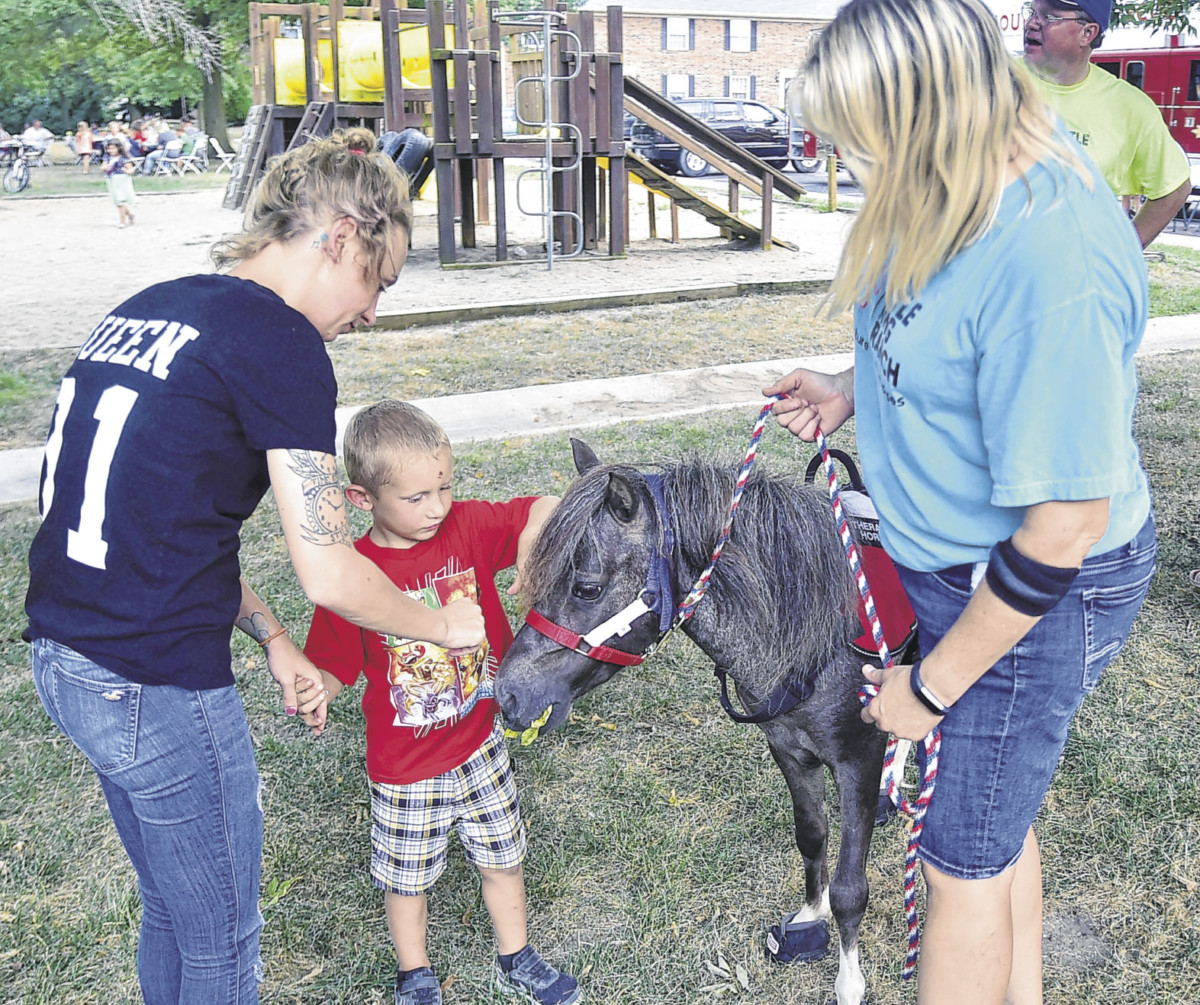 Haley Bannister, left, and Eli Hawn, 4, center, pet Flash the miniature therapy horse during the National Night Out event at Jamestown Apartments on Aug. 6. Also pictured is Kristye Lewis, who operates Little King Ranch Miniature Therapy Horses.